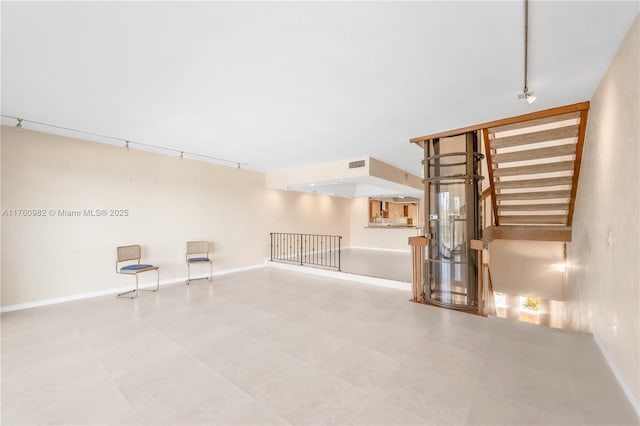 unfurnished living room with stairs, rail lighting, baseboards, and visible vents