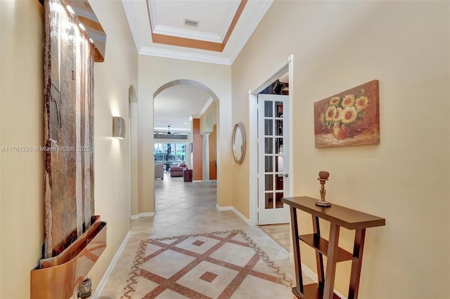 hallway with arched walkways, visible vents, crown molding, and baseboards