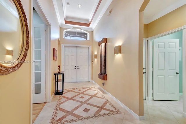 foyer entrance with a raised ceiling, arched walkways, crown molding, light tile patterned floors, and baseboards