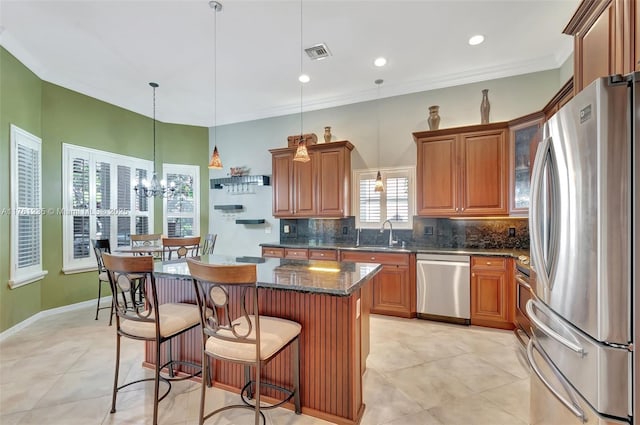 kitchen with brown cabinetry, visible vents, a kitchen island, appliances with stainless steel finishes, and tasteful backsplash