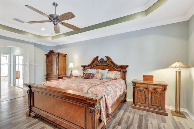 bedroom with arched walkways, light wood-type flooring, a tray ceiling, and ornamental molding