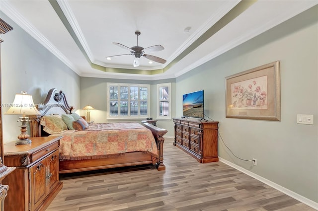 bedroom with a raised ceiling, crown molding, light wood-style floors, and baseboards