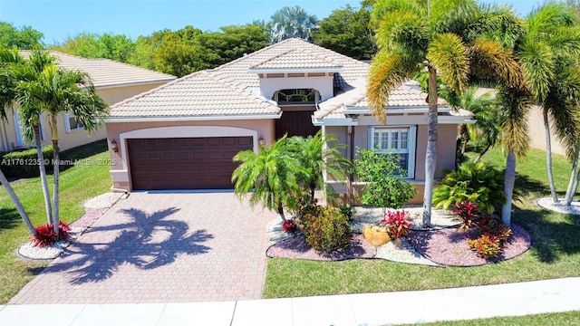 mediterranean / spanish house featuring a tiled roof, a front yard, stucco siding, decorative driveway, and a garage