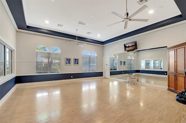 exercise room featuring visible vents, a raised ceiling, plenty of natural light, and wood finished floors