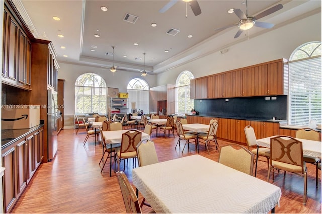 dining area with a raised ceiling, light wood-style floors, and visible vents