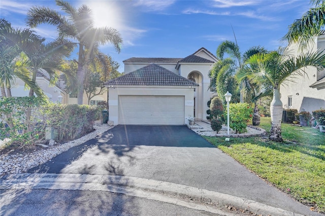 mediterranean / spanish-style house featuring aphalt driveway, a tile roof, a front yard, stucco siding, and a garage