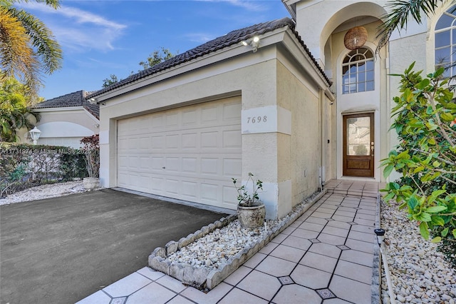 entrance to property with stucco siding, driveway, and a tiled roof