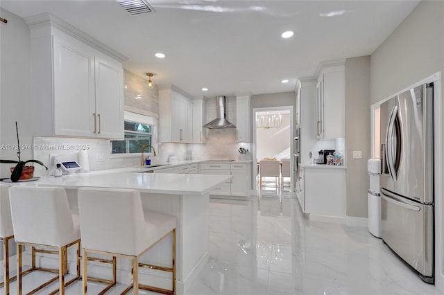 kitchen with visible vents, a peninsula, decorative backsplash, stainless steel refrigerator with ice dispenser, and wall chimney exhaust hood