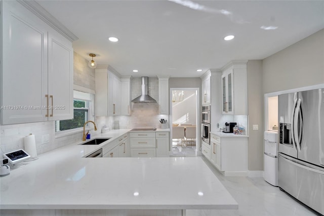 kitchen with tasteful backsplash, appliances with stainless steel finishes, white cabinets, wall chimney exhaust hood, and a sink