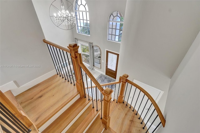 staircase with a high ceiling, a notable chandelier, wood finished floors, and baseboards