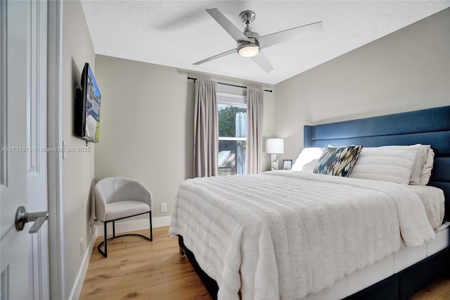 bedroom featuring a textured ceiling, light wood-style flooring, baseboards, and ceiling fan