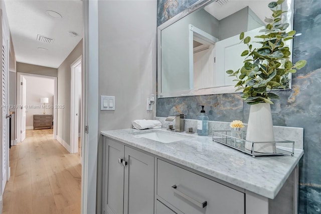 bathroom with visible vents, baseboards, decorative backsplash, wood finished floors, and vanity