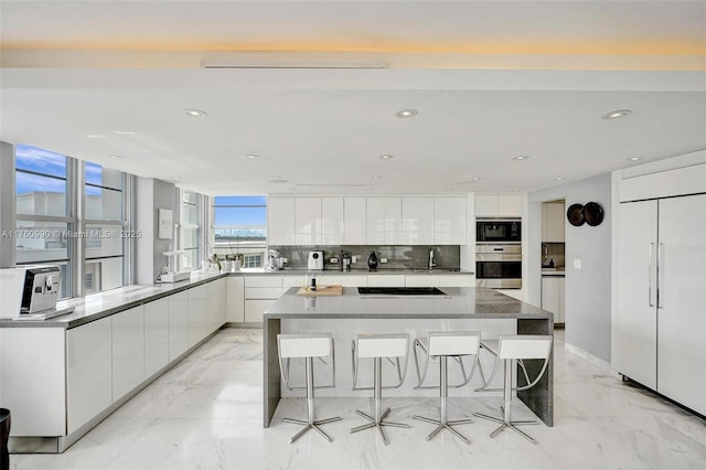 kitchen featuring marble finish floor, modern cabinets, a kitchen breakfast bar, white cabinets, and built in appliances