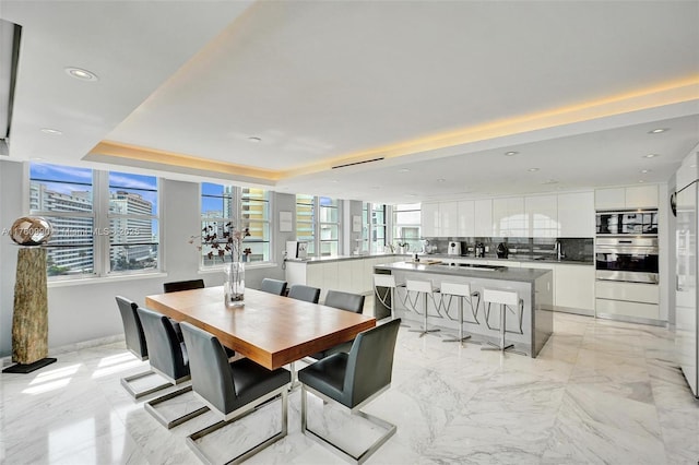 dining area with a raised ceiling, recessed lighting, and marble finish floor