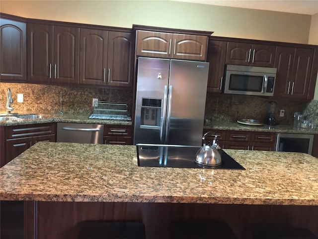 kitchen with tasteful backsplash, dark brown cabinetry, light stone counters, appliances with stainless steel finishes, and a sink