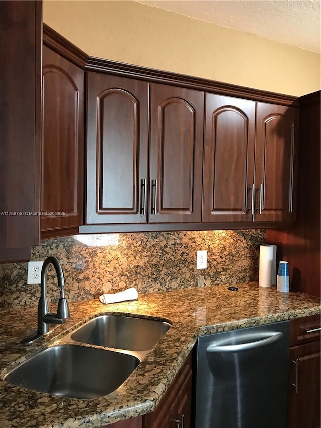 kitchen with dark brown cabinetry, a sink, dark stone countertops, and stainless steel dishwasher
