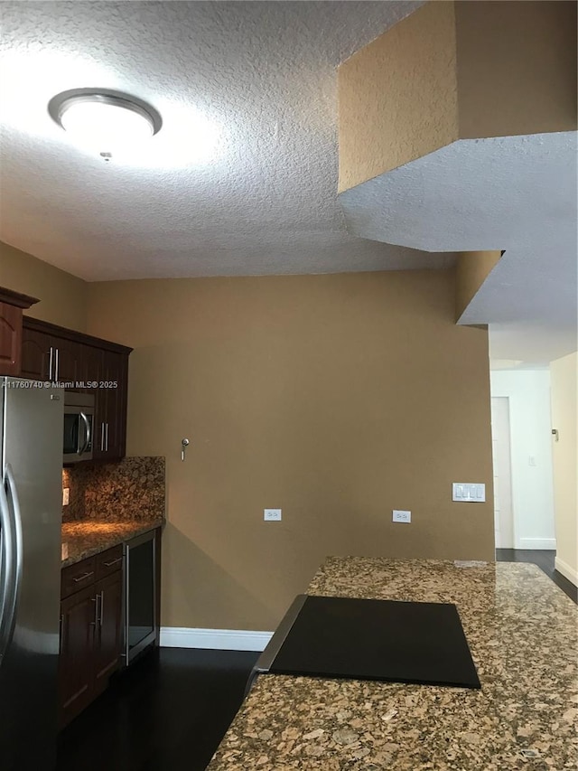 kitchen with baseboards, dark stone counters, dark brown cabinets, appliances with stainless steel finishes, and a textured ceiling