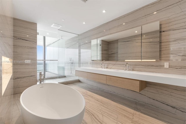 bathroom with stone wall, a soaking tub, double vanity, a sink, and tile walls