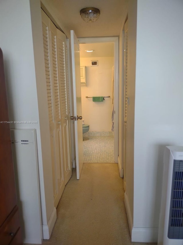 corridor with heating unit, visible vents, light carpet, and baseboards