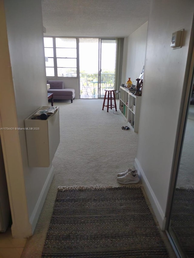 hall with carpet flooring, floor to ceiling windows, a textured ceiling, and baseboards