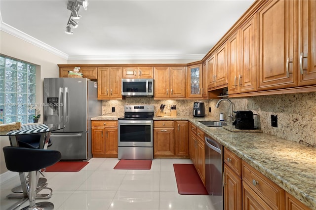 kitchen with tasteful backsplash, ornamental molding, brown cabinets, stainless steel appliances, and a sink