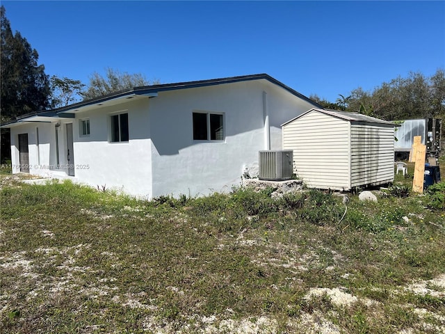 view of side of property with stucco siding, an outbuilding, and central AC unit