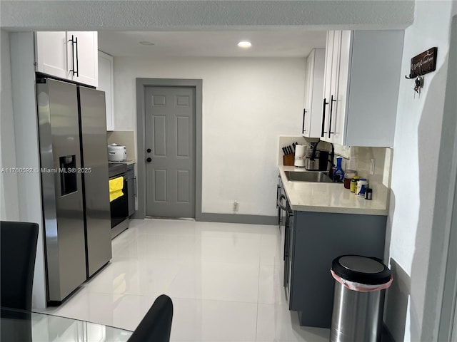 kitchen with stainless steel refrigerator with ice dispenser, a sink, light countertops, light tile patterned floors, and range