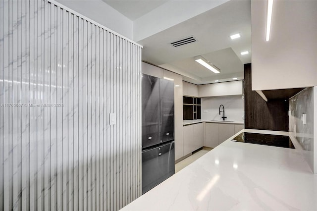 kitchen featuring visible vents, light countertops, white cabinetry, black electric cooktop, and a sink