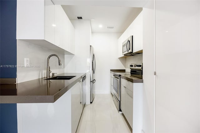 kitchen with a sink, modern cabinets, dark countertops, and appliances with stainless steel finishes