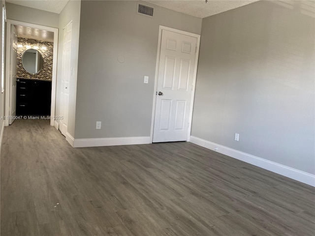 unfurnished bedroom featuring a textured ceiling, dark wood-style floors, visible vents, and baseboards