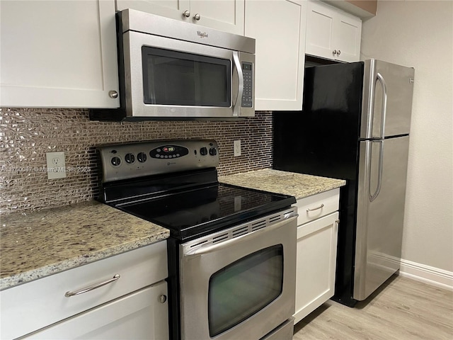 kitchen featuring light stone counters, white cabinets, appliances with stainless steel finishes, light wood-type flooring, and backsplash