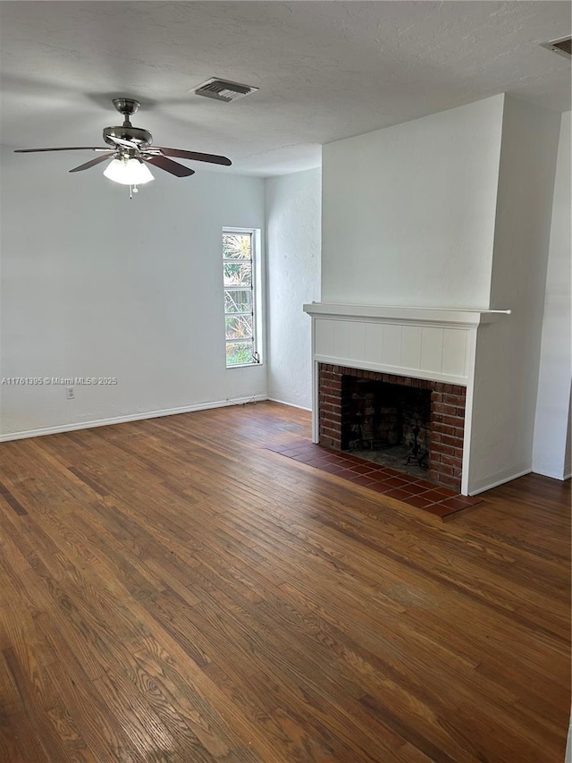 unfurnished living room with a ceiling fan, wood finished floors, visible vents, a textured ceiling, and a tiled fireplace