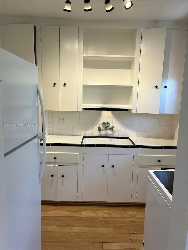 kitchen featuring tile countertops, light wood-style flooring, freestanding refrigerator, white cabinetry, and a sink