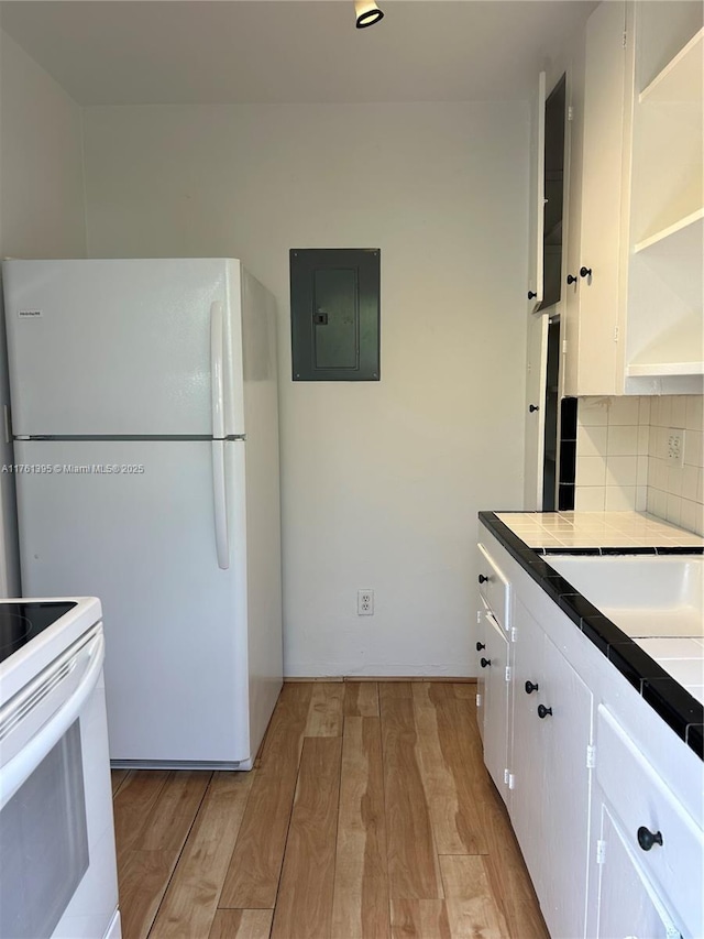 kitchen with light wood-type flooring, electric panel, tile countertops, white appliances, and white cabinets