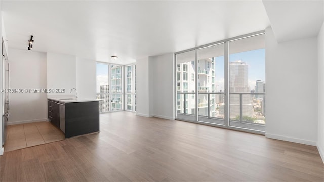 spare room featuring light wood-type flooring, expansive windows, a view of city, and baseboards