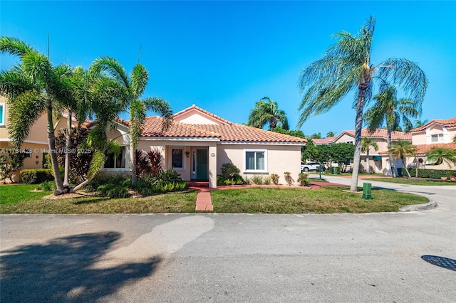 mediterranean / spanish house featuring a tile roof, a front lawn, and stucco siding