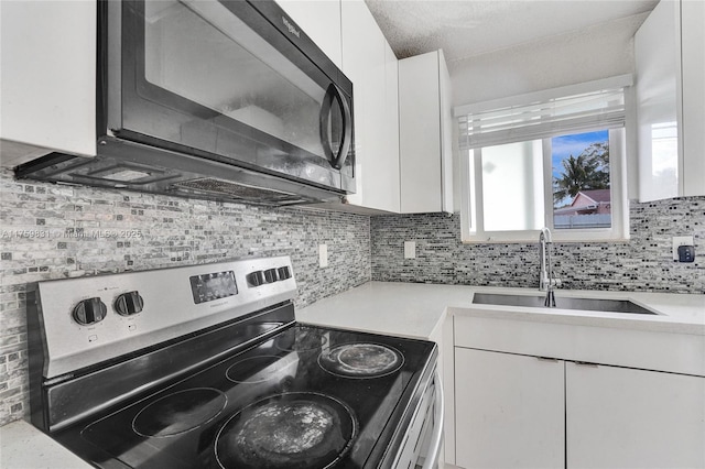 kitchen featuring tasteful backsplash, black microwave, stainless steel electric range oven, white cabinets, and a sink