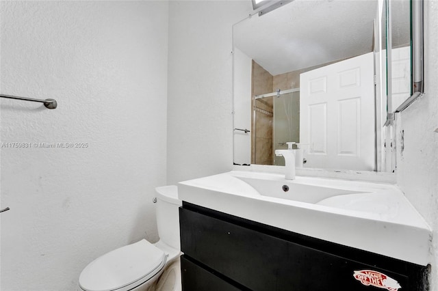 full bath featuring toilet, a stall shower, vanity, and a textured wall