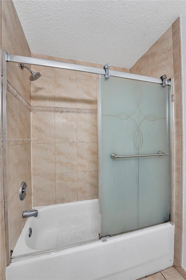 bathroom featuring combined bath / shower with glass door and a textured ceiling