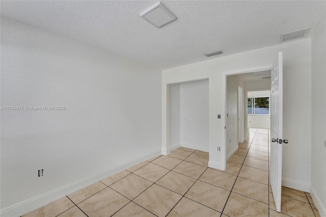 spare room featuring light tile patterned floors, visible vents, a textured ceiling, and baseboards