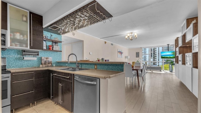 kitchen with a sink, tile countertops, appliances with stainless steel finishes, a peninsula, and decorative backsplash