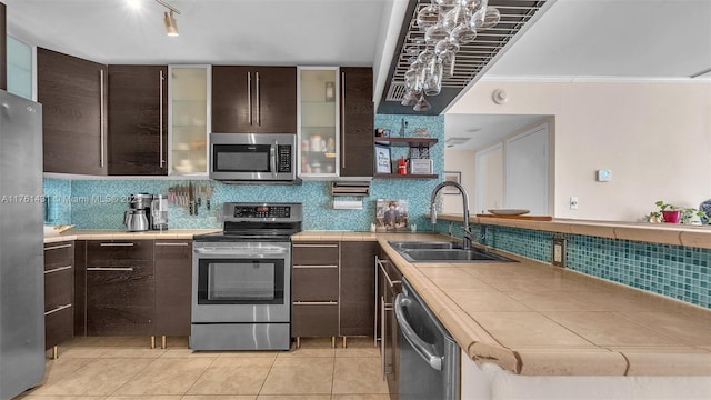 kitchen with dark brown cabinetry, a sink, stainless steel appliances, and tile counters