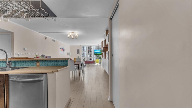 kitchen featuring tile counters, dishwasher, light wood-type flooring, an inviting chandelier, and a sink