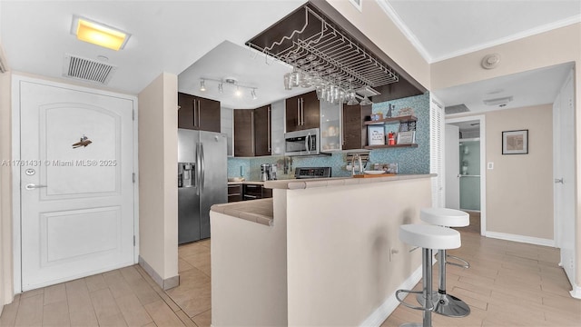 kitchen featuring visible vents, dark brown cabinetry, decorative backsplash, appliances with stainless steel finishes, and a kitchen breakfast bar