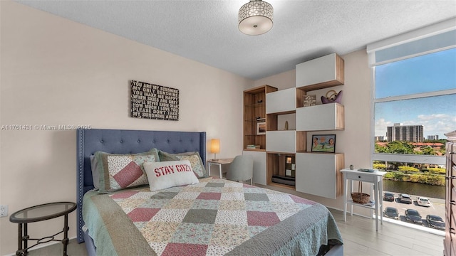 bedroom with expansive windows, a textured ceiling, a city view, and wood finished floors