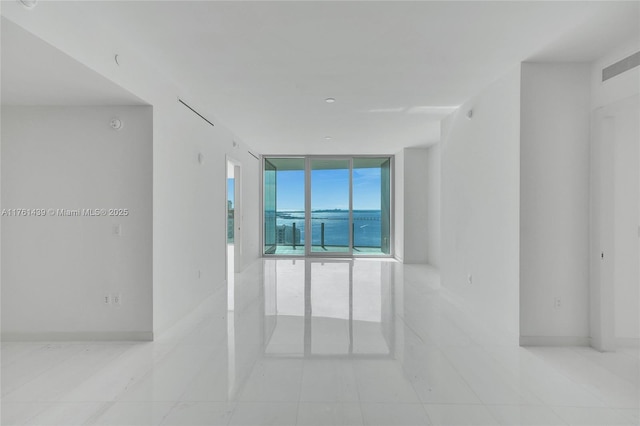 empty room featuring visible vents, a wall of windows, and baseboards