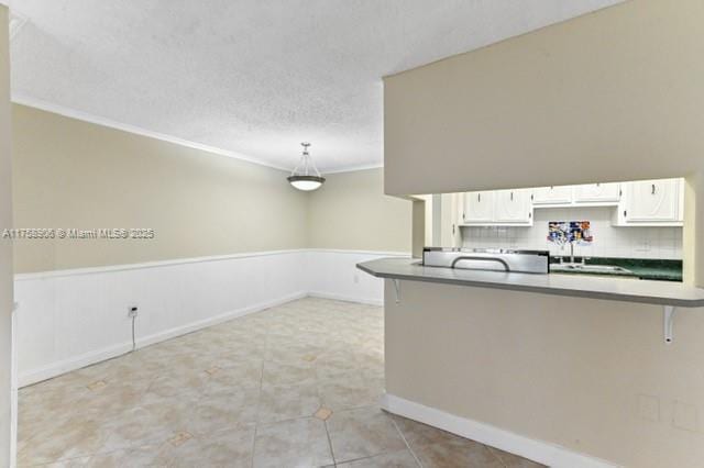 kitchen with white cabinetry, crown molding, a breakfast bar area, decorative backsplash, and a textured ceiling