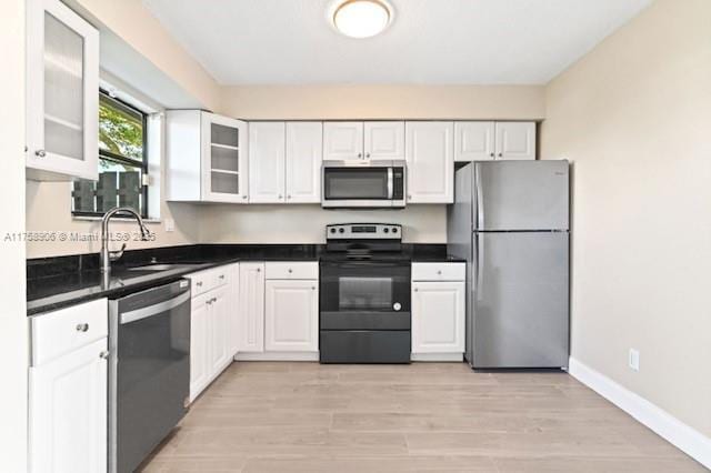 kitchen featuring dark countertops, baseboards, stainless steel appliances, light wood-style floors, and white cabinetry