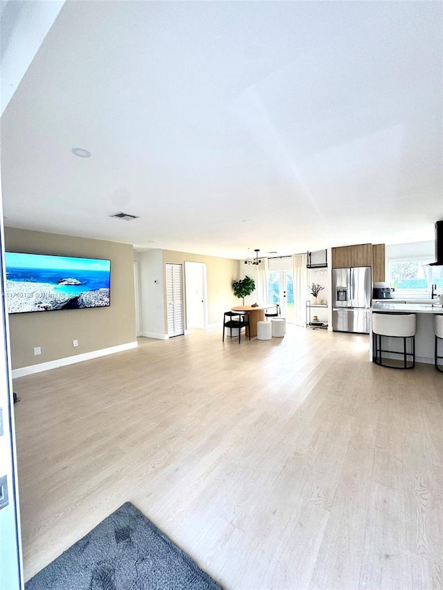 unfurnished living room with visible vents, light wood-style flooring, and baseboards