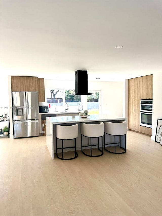 kitchen featuring a kitchen bar, light wood-style flooring, brown cabinetry, stainless steel appliances, and modern cabinets